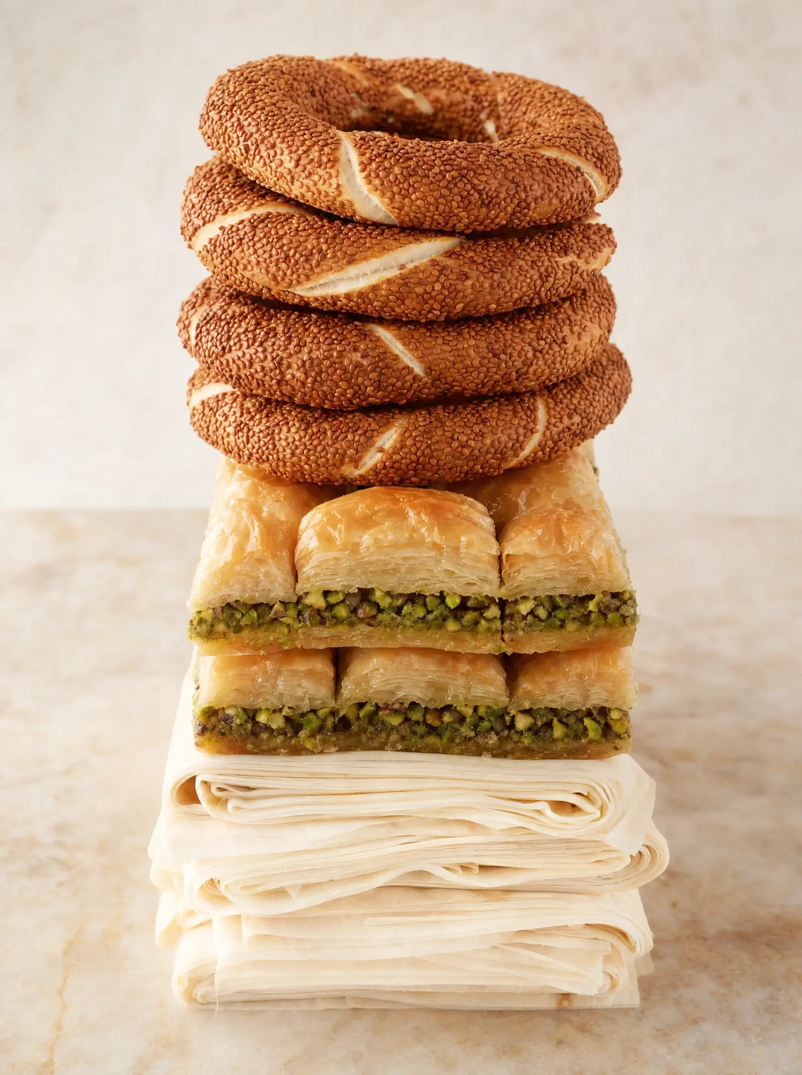 Sesame simit rings stacked above layered pistachio baklava and folded filo pastry sheets