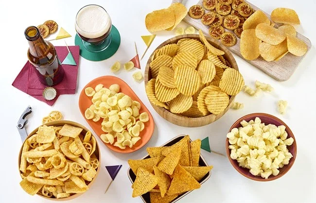 Assorted savoury snacks including crisps, crackers, popcorn and nuts