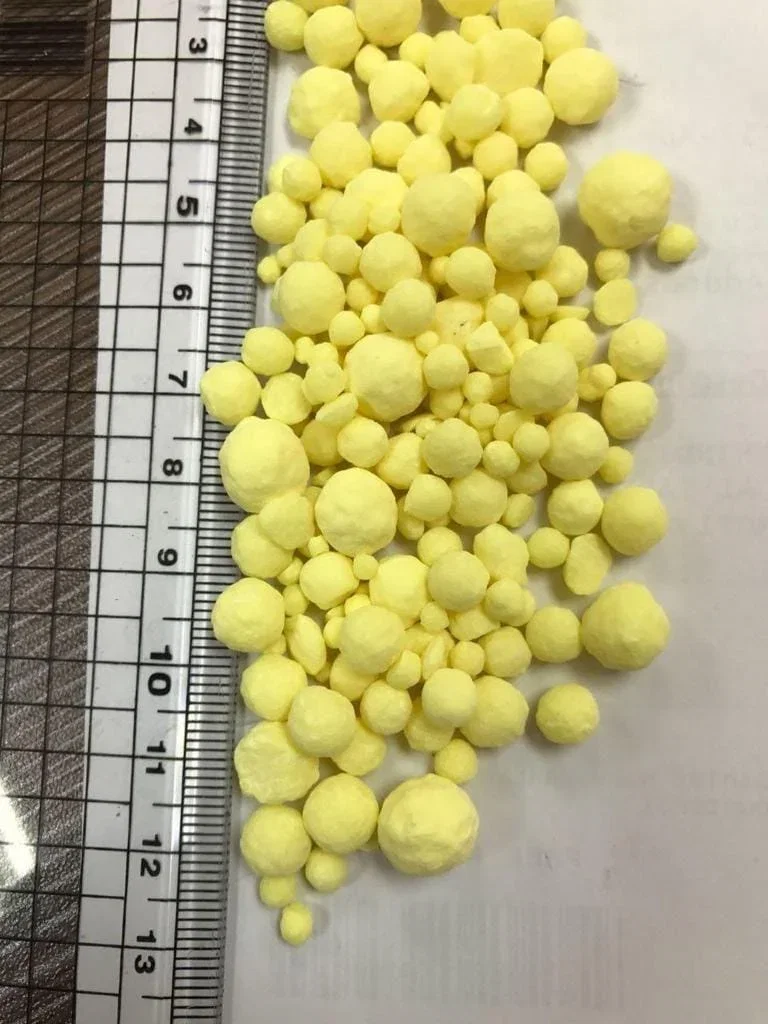 Granulated sulfur pastilles measured against a millimetre rule