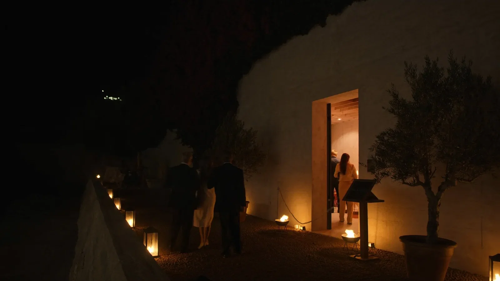 A discreet lantern-lit entrance to an exclusive seaside venue at night with a rope line and host stand