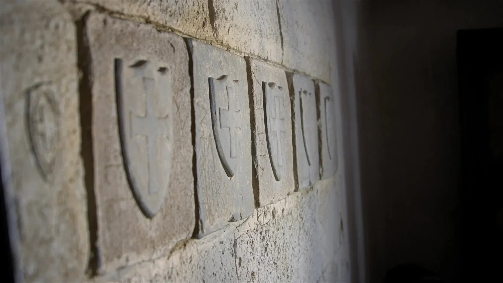 Weathered carved coats of arms of the Knights of St John set into a limestone castle wall