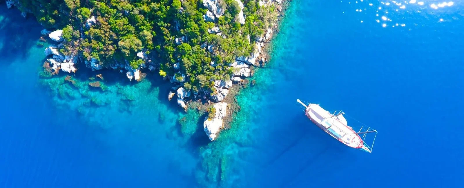 Aerial view of the Bodrum coastline with turquoise coves and a sailing yacht