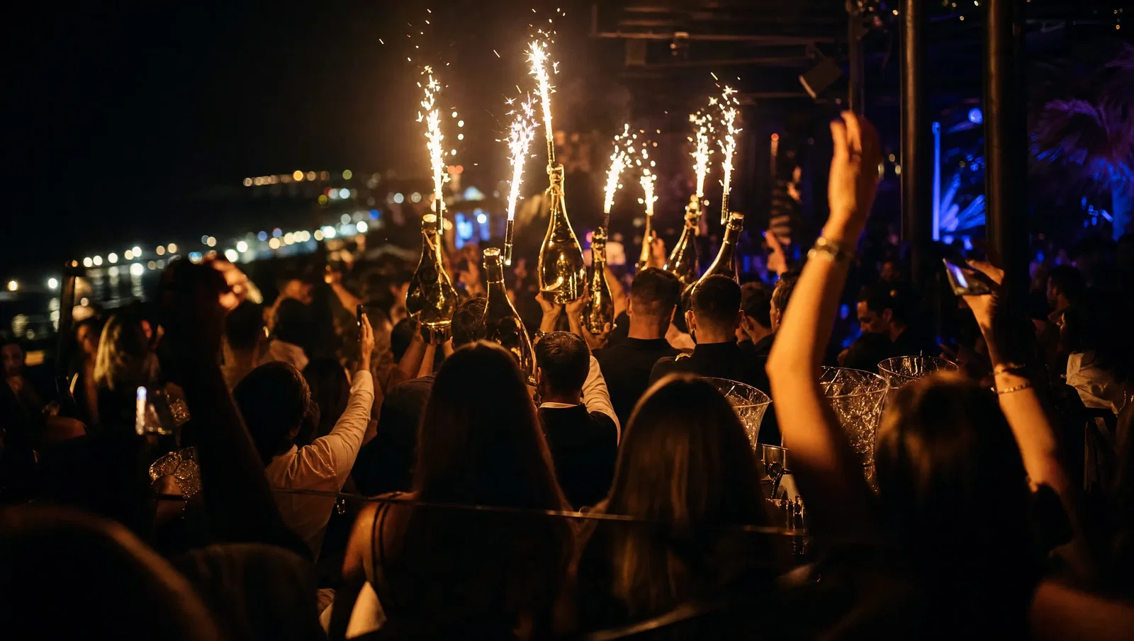 Bottles carried through a crowded seaside club with sparkler fountains lighting the room